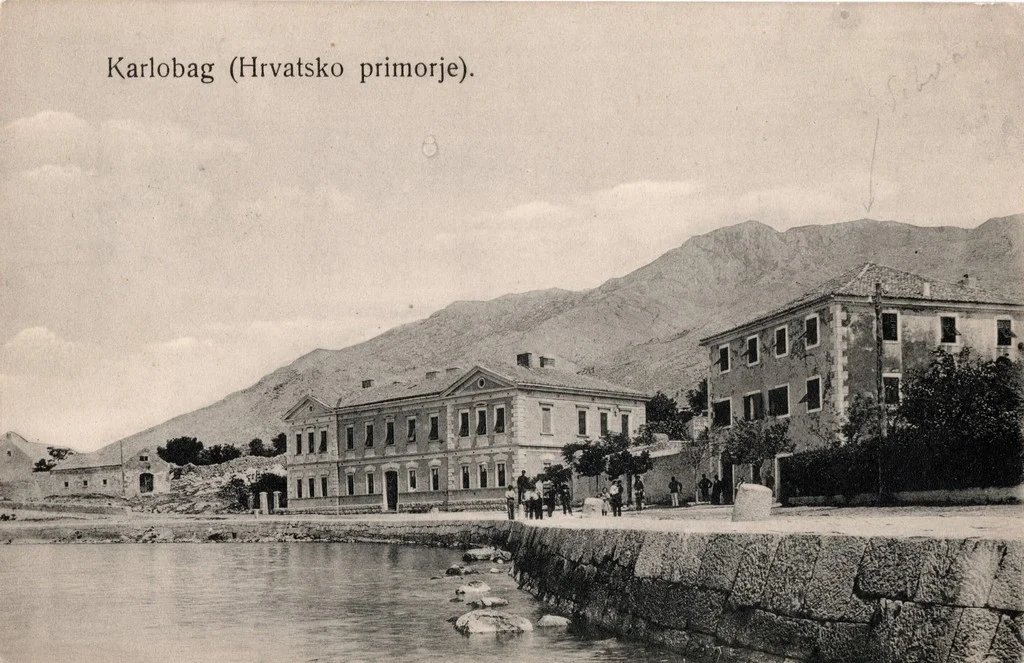 Crno-bijela povijesna razglednica škole na obali Karlobaga, s Velebitom u pozadini